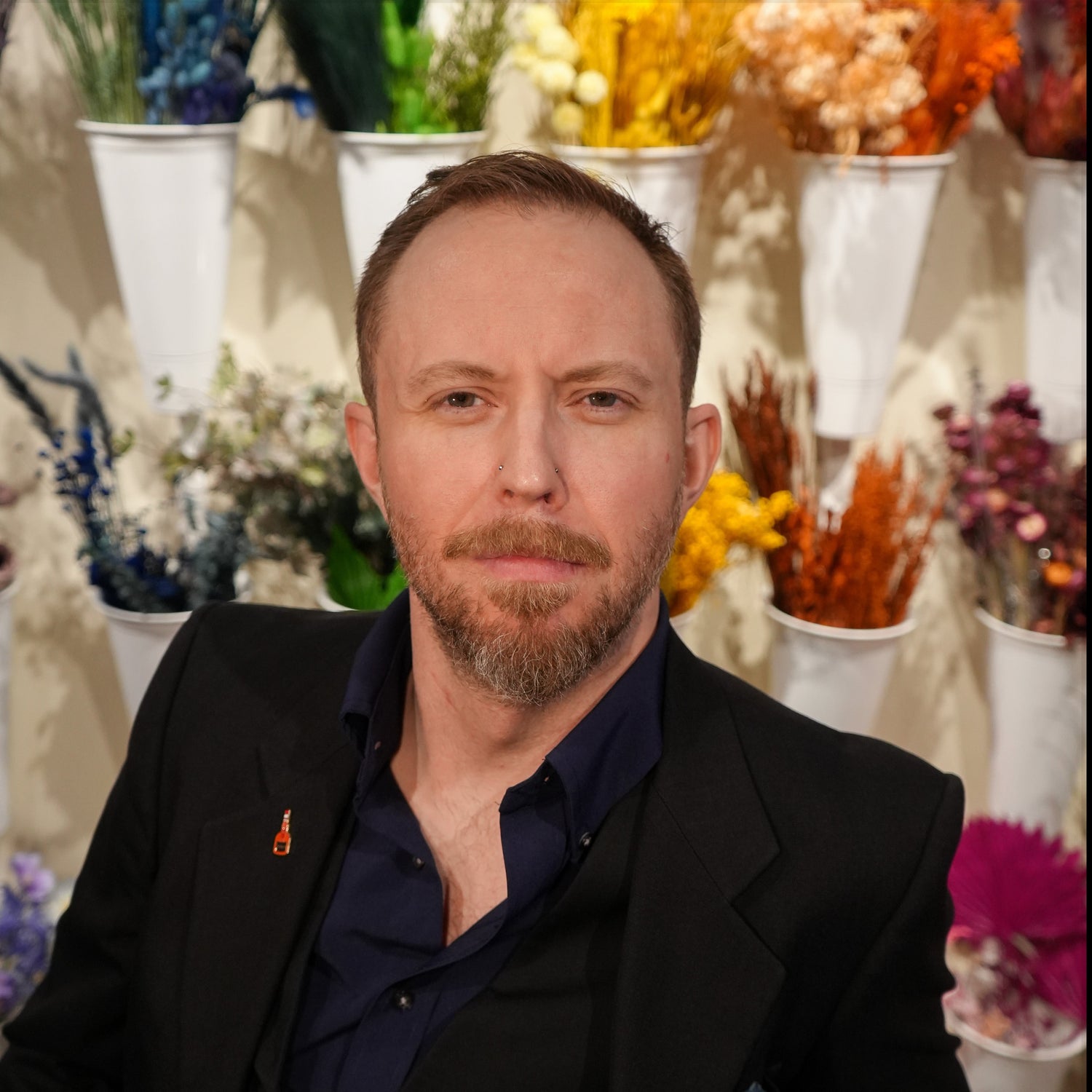 Man with a beard and mustache in front of floral arrangements